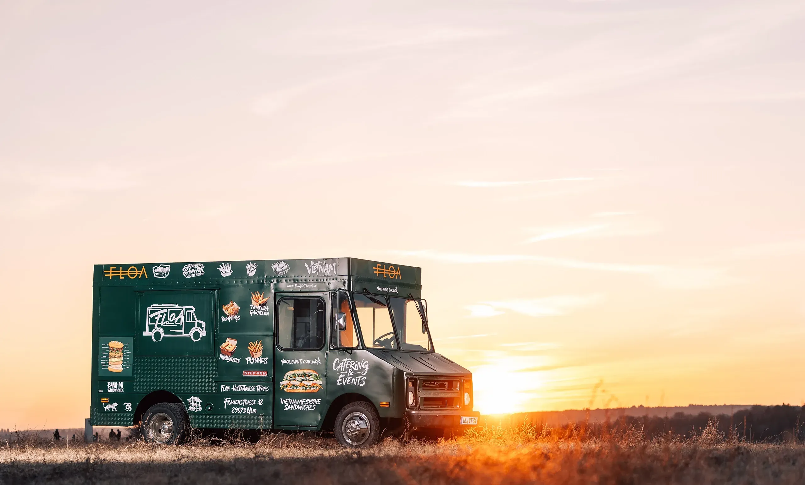 Der FLOA Foodtruck steht auf einem Feld - im Hintergrund ist der Sonnenuntergang